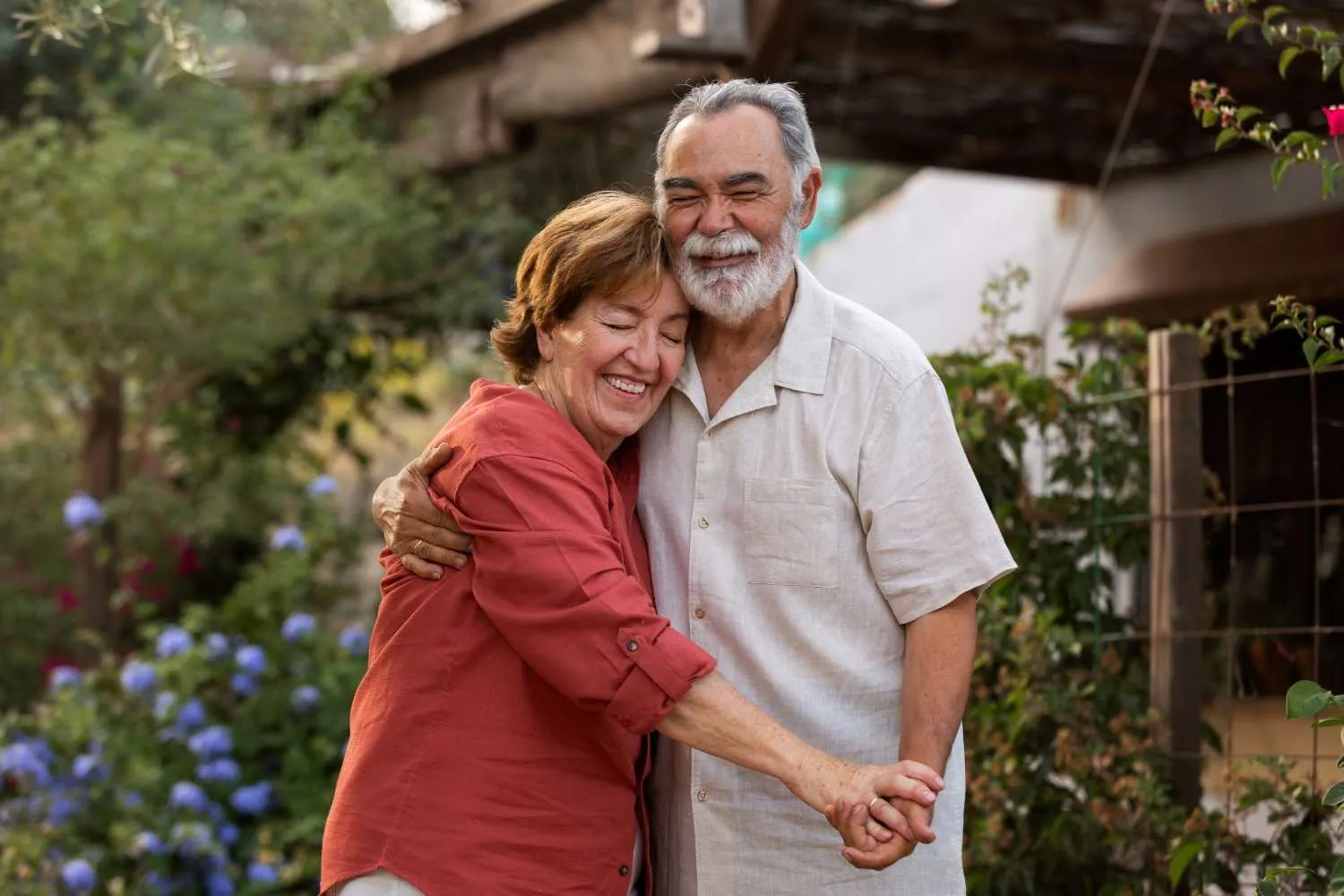 An older couple laughing and holding each other in a garden